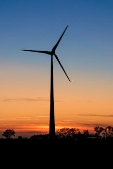 A lone wind turbine silhouetted against a vibrant sunset sky, symbolizing renewable energy.
